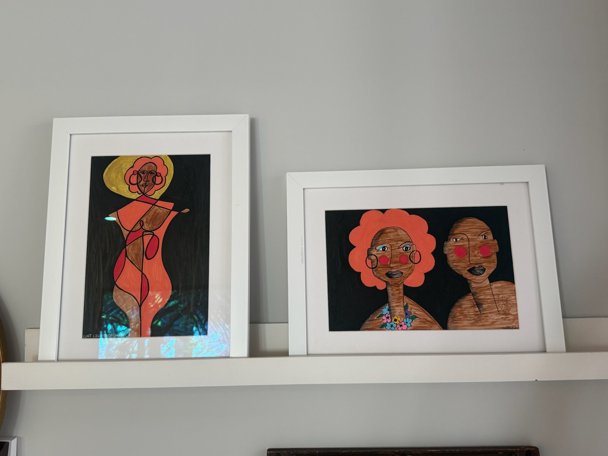 Framed abstract figure artwork on shelf